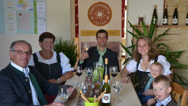 Familie in traditioneller Kleidung sitzt an einem Tisch mit Wein und Gläsern.