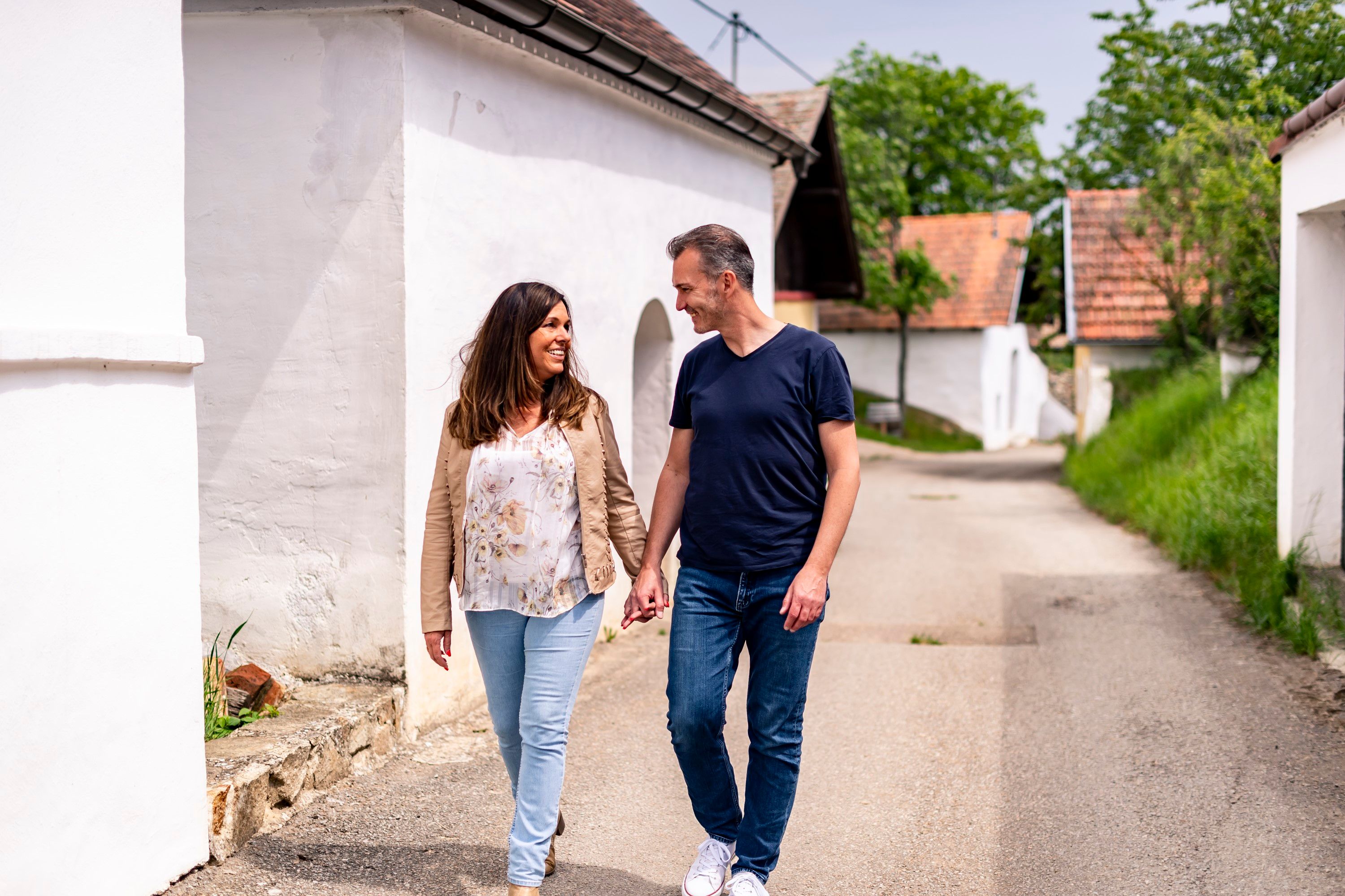 Ein Paar spaziert Hand in Hand durch die Öhlbergkellergasse in Pillersdorf, umgeben von traditionellen Weinkellern und grüner Landschaft.