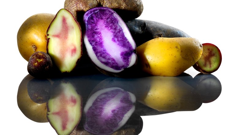 Different types of potatoes, some sliced, on a reflective surface.