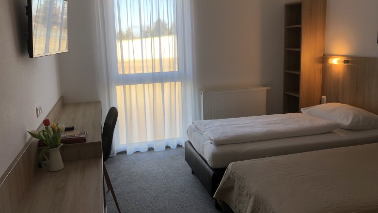 Ein schlicht eingerichtetes Motelzimmer mit zwei Einzelbetten, einem Schreibtisch, einem Fernseher und einem Fenster mit Vorhängen.