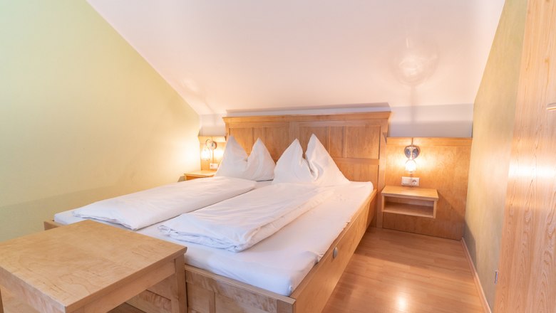 Gemütliches Schlafzimmer mit Holzmöbeln und Doppelbett unter einer Dachschräge.