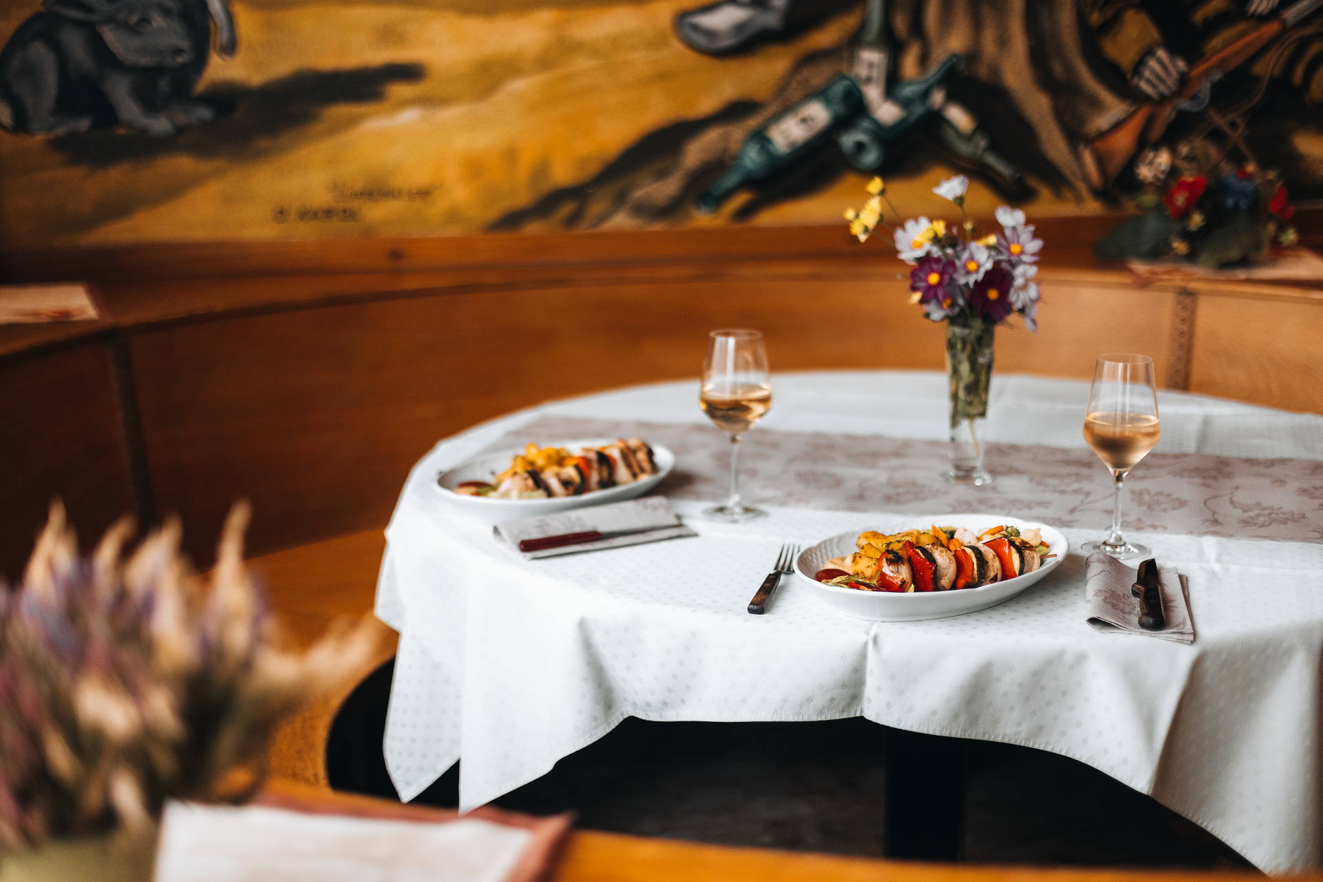 Ein einladender Tisch in einem gemütlichen Wirtshaus, geschmückt mit frischen Blumen und köstlichen Speisen, lädt zum Verweilen ein. Die sanfte Beleuchtung und die rustikale Atmosphäre schaffen eine perfekte Kulisse für gesellige Stunden mit Freunden und Familie. Hier wird die Wirtshauskultur Niederösterreichs in vollen Zügen genossen.