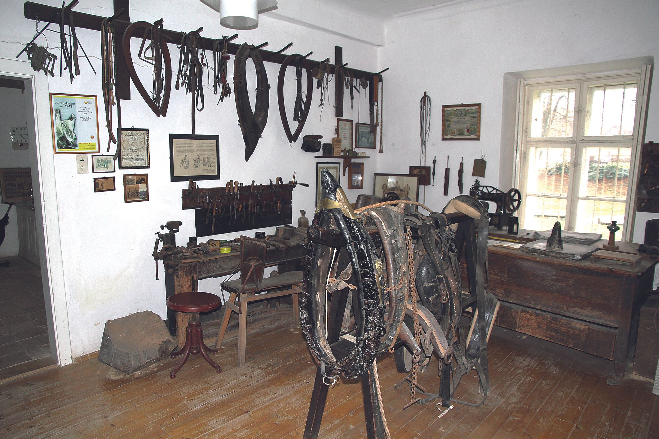 Miestnosť v miestnom historickom múzeu so starým náradím a konskými postrojmi na stenách.