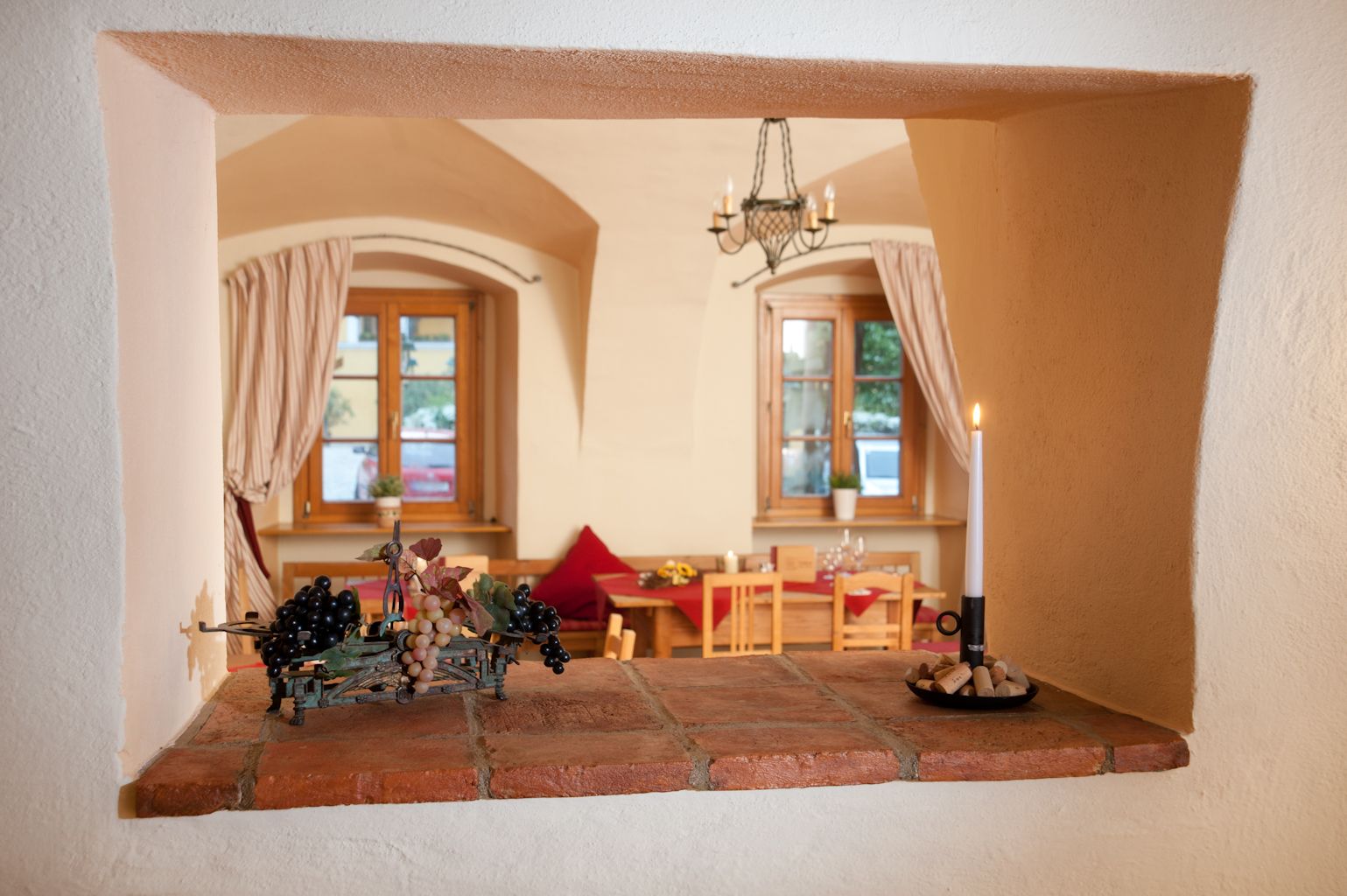 Blick durch eine Maueröffnung in einen gemütlichen Raum mit Holzmöbeln und Kerzenlicht.