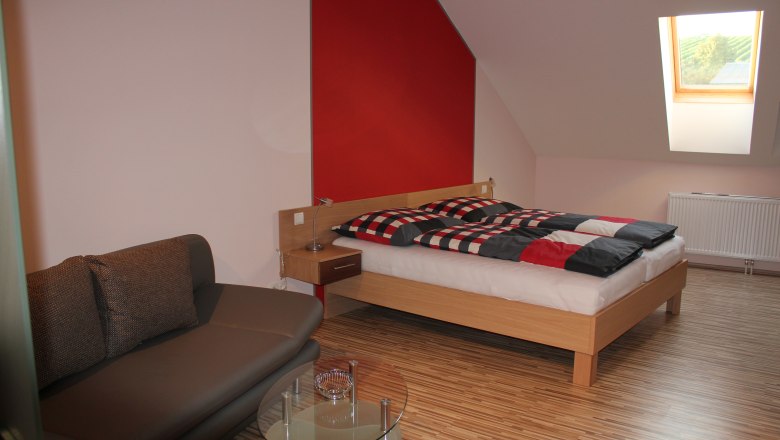 Modern eingerichtetes Gästezimmer mit Bett, Sofa und Dachfenster.