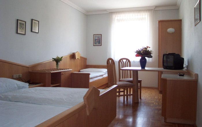 Ein einfach eingerichtetes Hotelzimmer mit zwei Betten, einem Tisch, Stühlen und einem kleinen Fernseher.