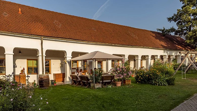 Weingut Bohrn, © Robert Herbst Ein traditionelles Weingut mit weißen Arkaden, einem roten Ziegeldach und einem Garten mit Sitzbereich und Blumen.