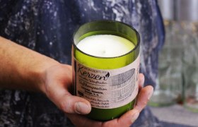 Eine Hand hält eine grüne Duftkerze mit Etikett 'Weinviertler Kerzen'.