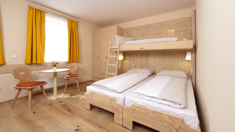 Gemütliches Gästezimmer mit Etagenbett, Holzmöbeln und gelben Vorhängen.