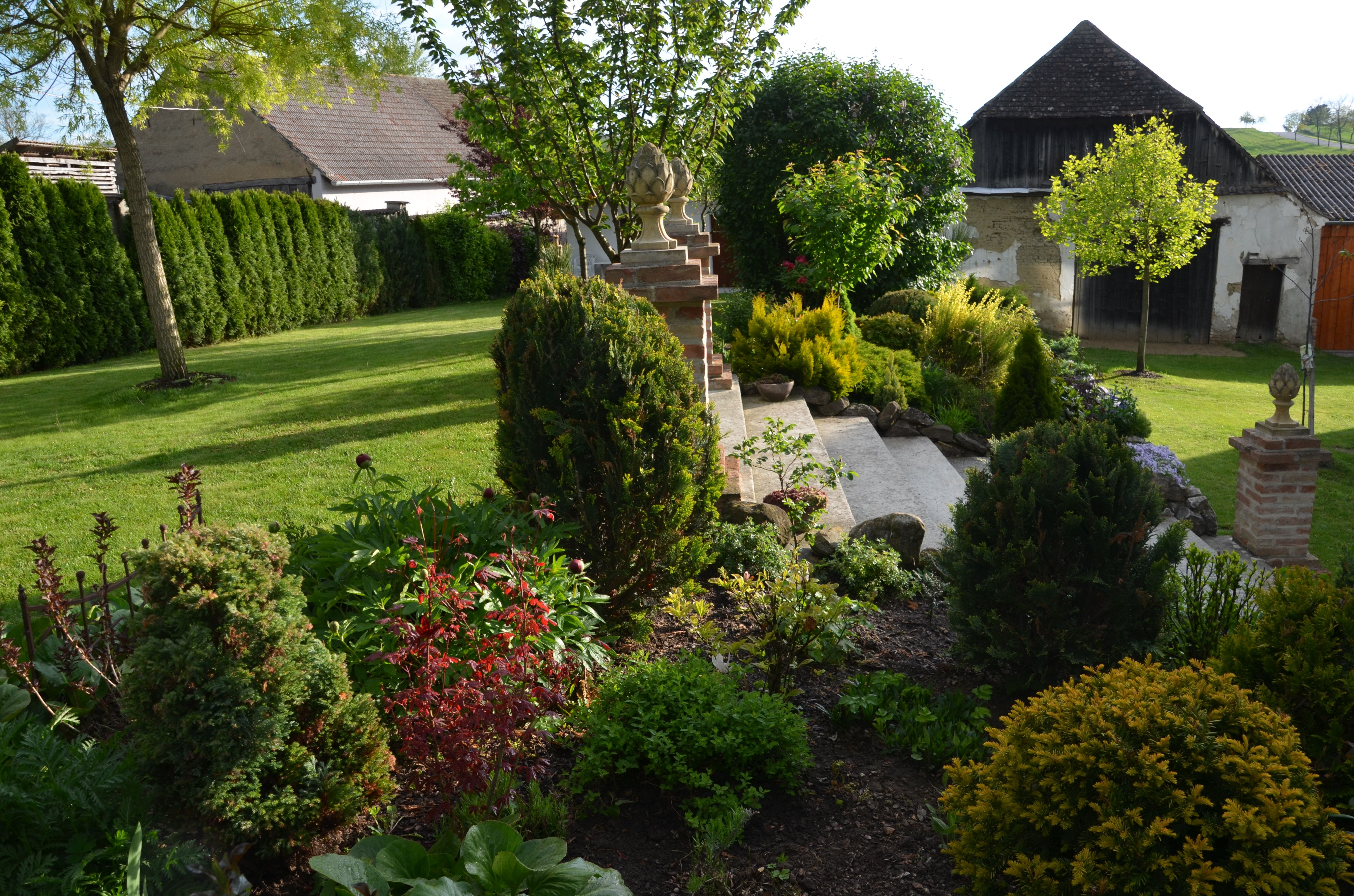 A well-kept garden with lawn, bushes and trees, surrounded by buildings in the background.