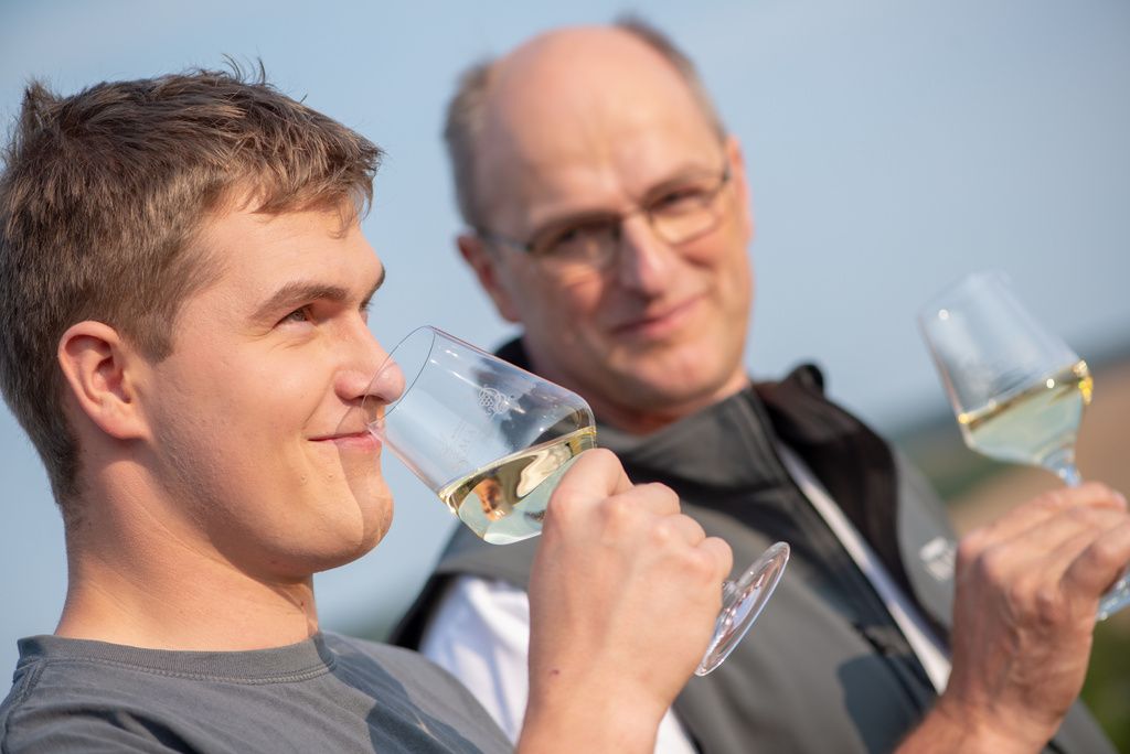 Two men enjoy white wine outdoors.