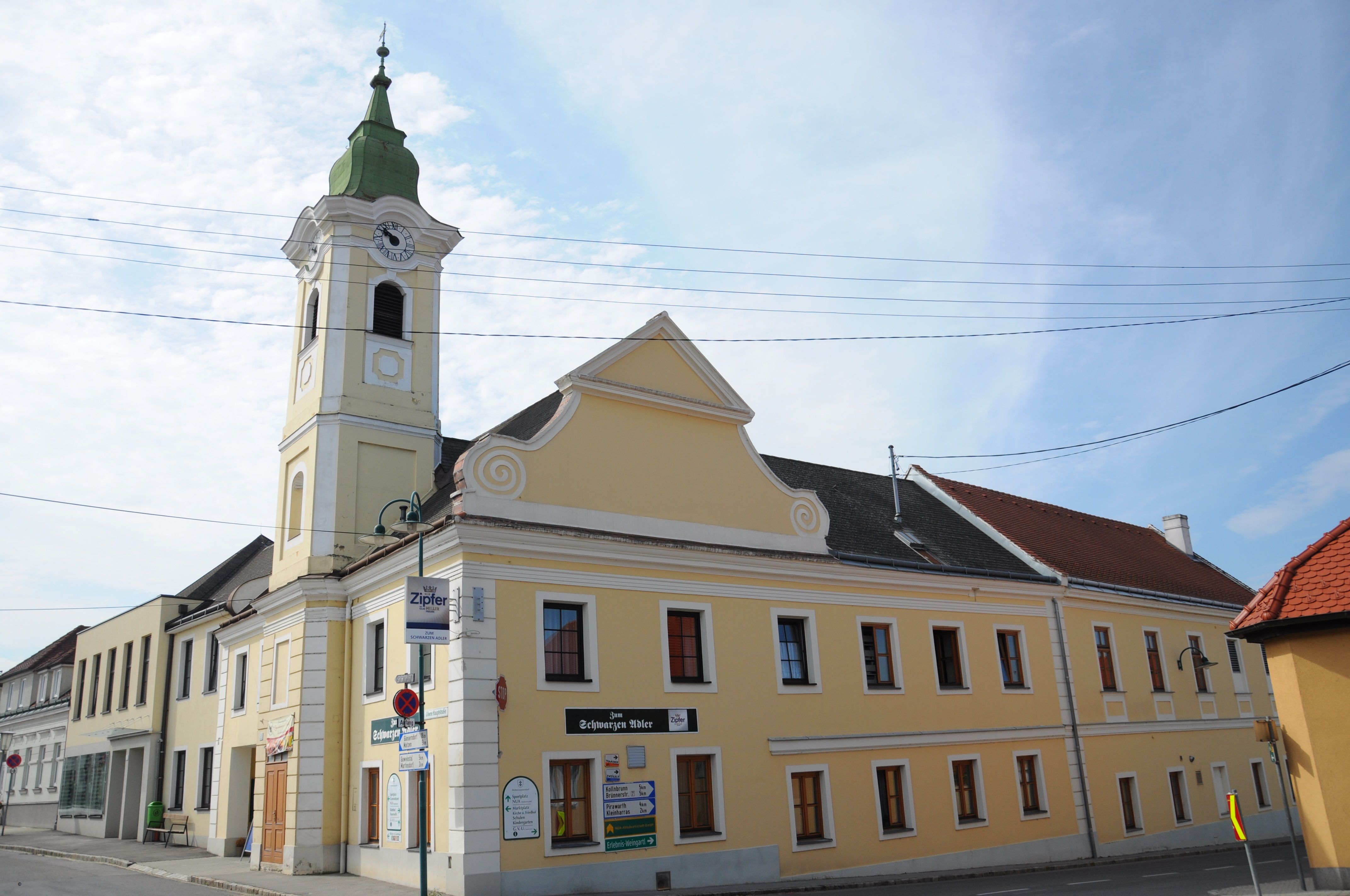 Gelbes Gebäude mit Turm und Uhr, Gasthaus zum schwarzen Adler, blauer Himmel.