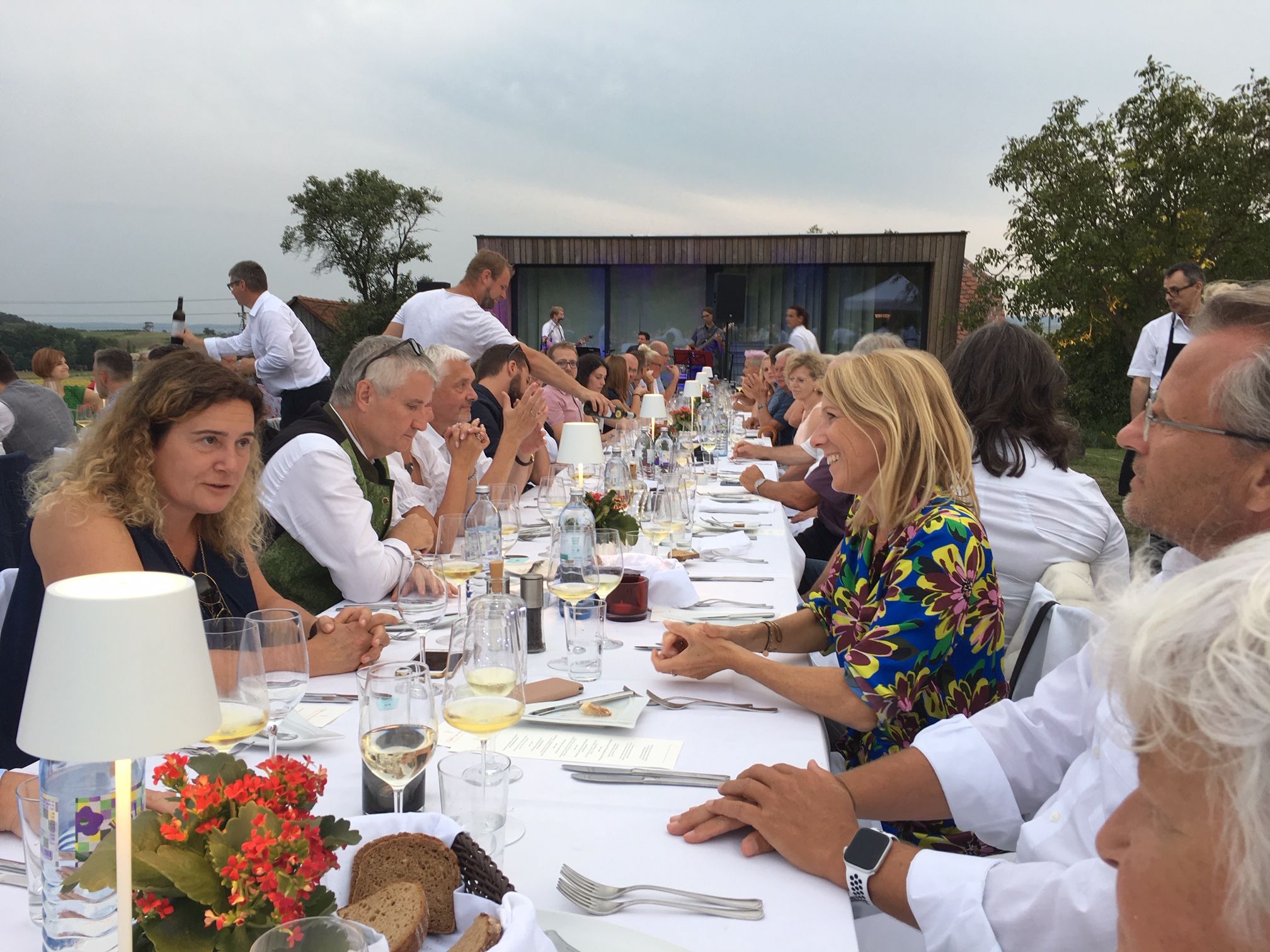 Menschen sitzen an einem langen Tisch im Freien und unterhalten sich bei einem festlichen Essen.