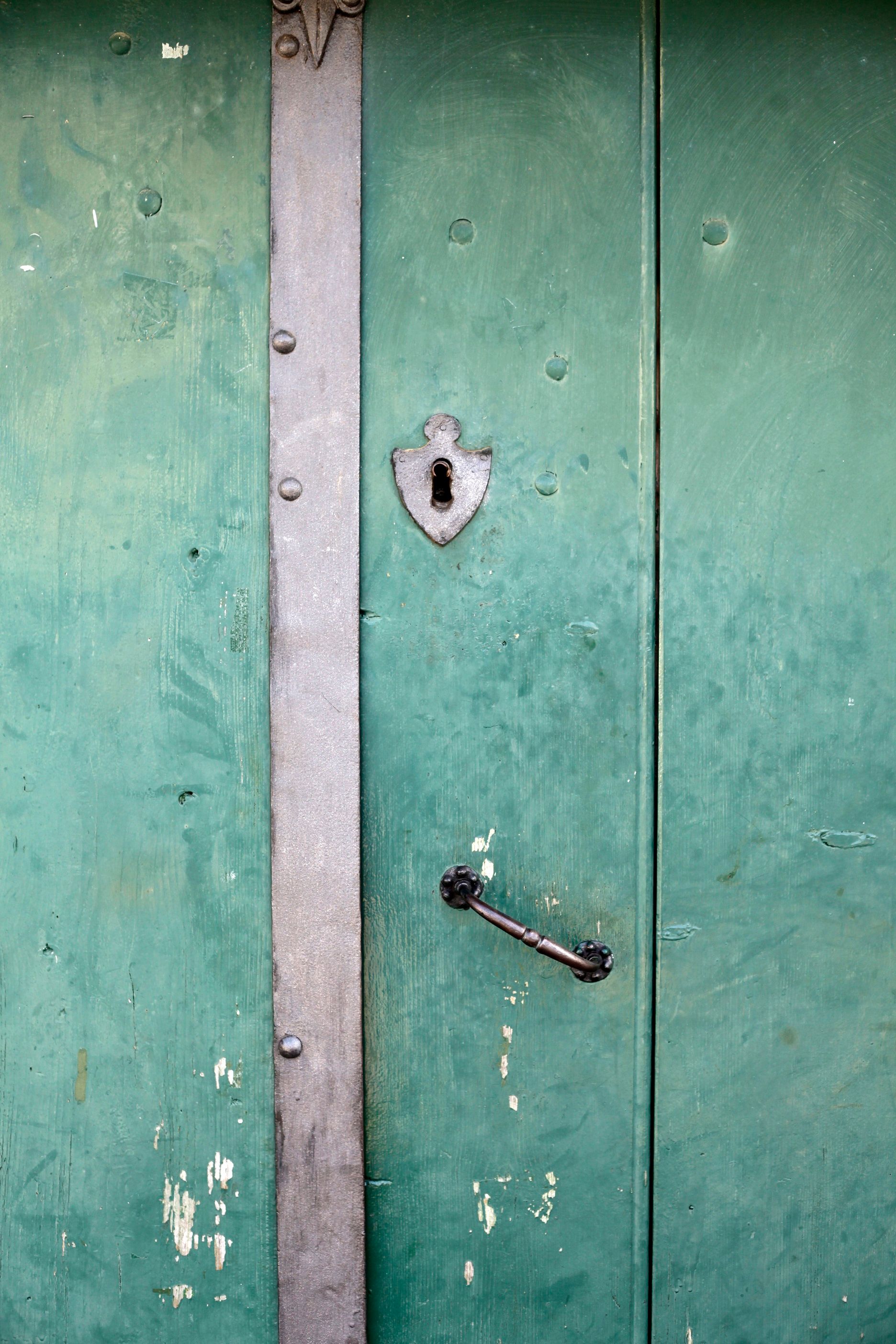 Grüne Holztür mit Metallbeschlägen und einem Schlüsselloch.
