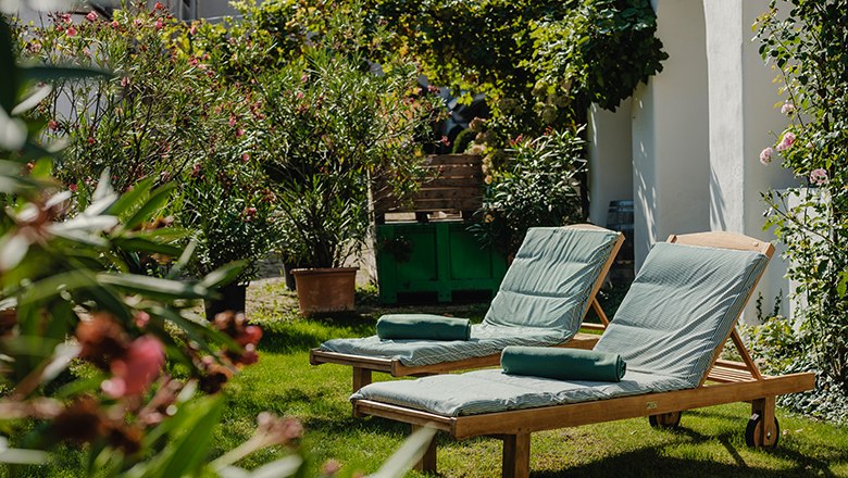 Two sun loungers in the green garden with plants and flowers.
