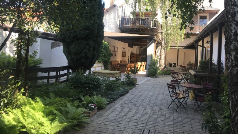 Ein ruhiger Innenhof mit Bäumen, Pflanzen und Gartenmöbeln unter blauem Himmel.