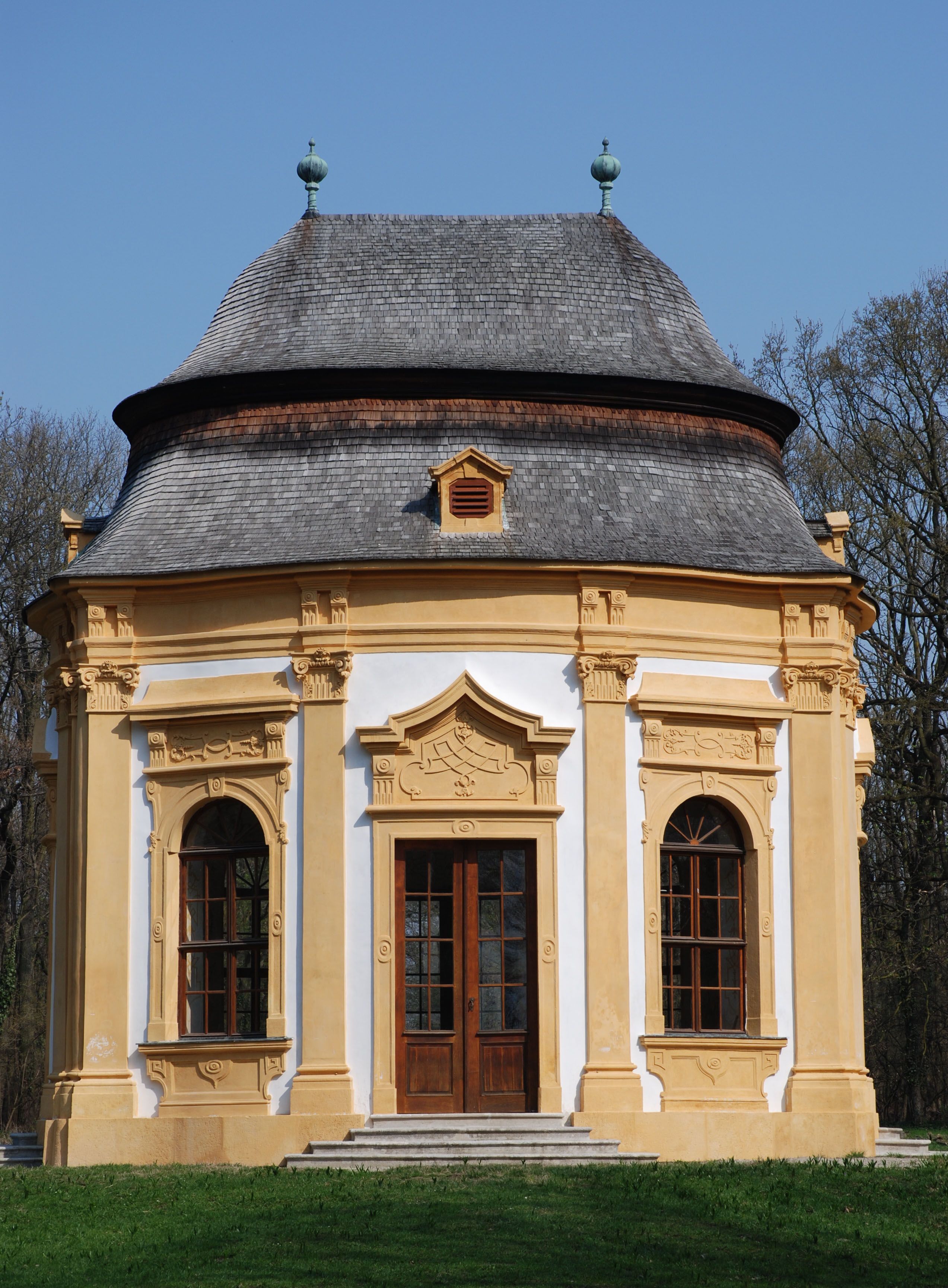 Baroque garden pavilion with yellow decorations and a gray roof against a blue sky.