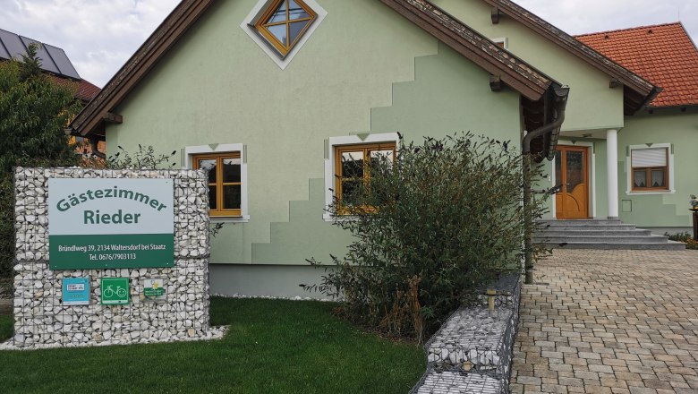 Grünes Haus mit Schild 'Gästezimmer Rieder' im Vorgarten.