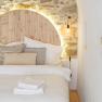 Cozy double bed with stone wall and wooden back wall, illuminated by a lamp.