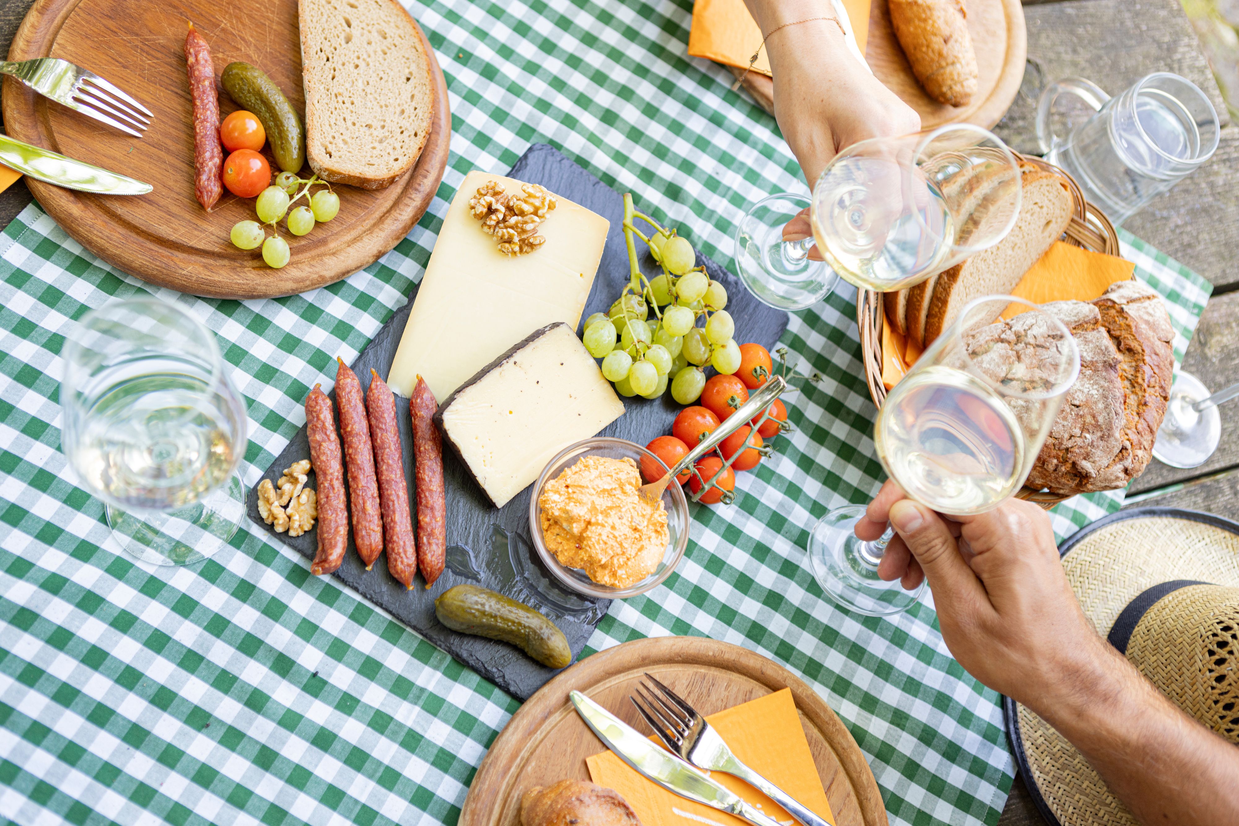 Picknick mit Käse, Wurst, Brot und Wein auf kariertem Tischtuch.