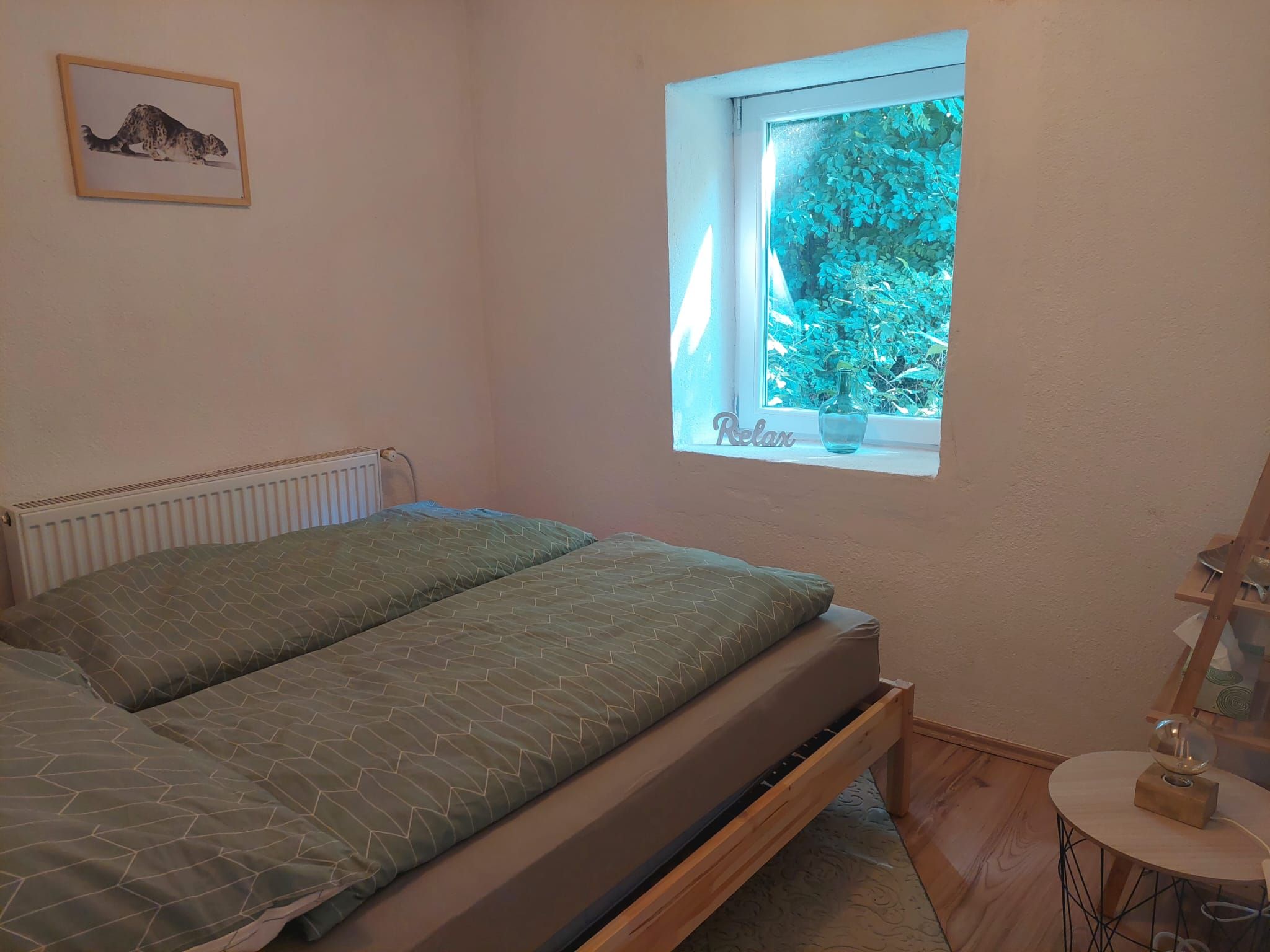 Ein gemütliches Schlafzimmer mit einem Bett, einem Fenster mit Blick ins Grüne und einem Bild an der Wand.