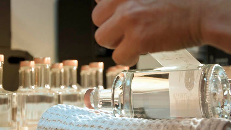 Nahaufnahme einer Hand, die ein Etikett auf eine Flasche Edelbrand klebt.