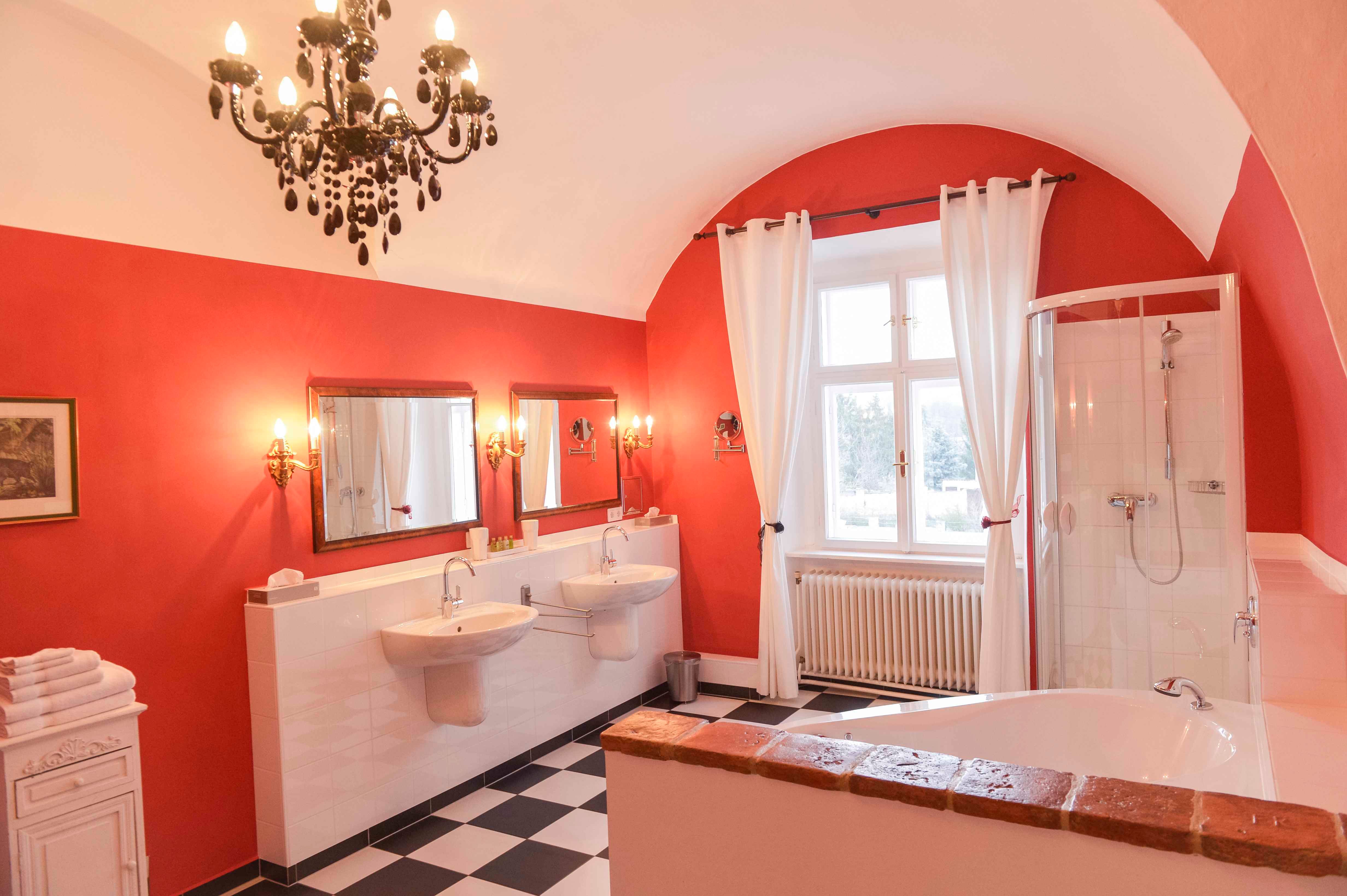 Elegantes Badezimmer mit roten Wänden, zwei Waschbecken, Badewanne, Dusche und Kronleuchter.