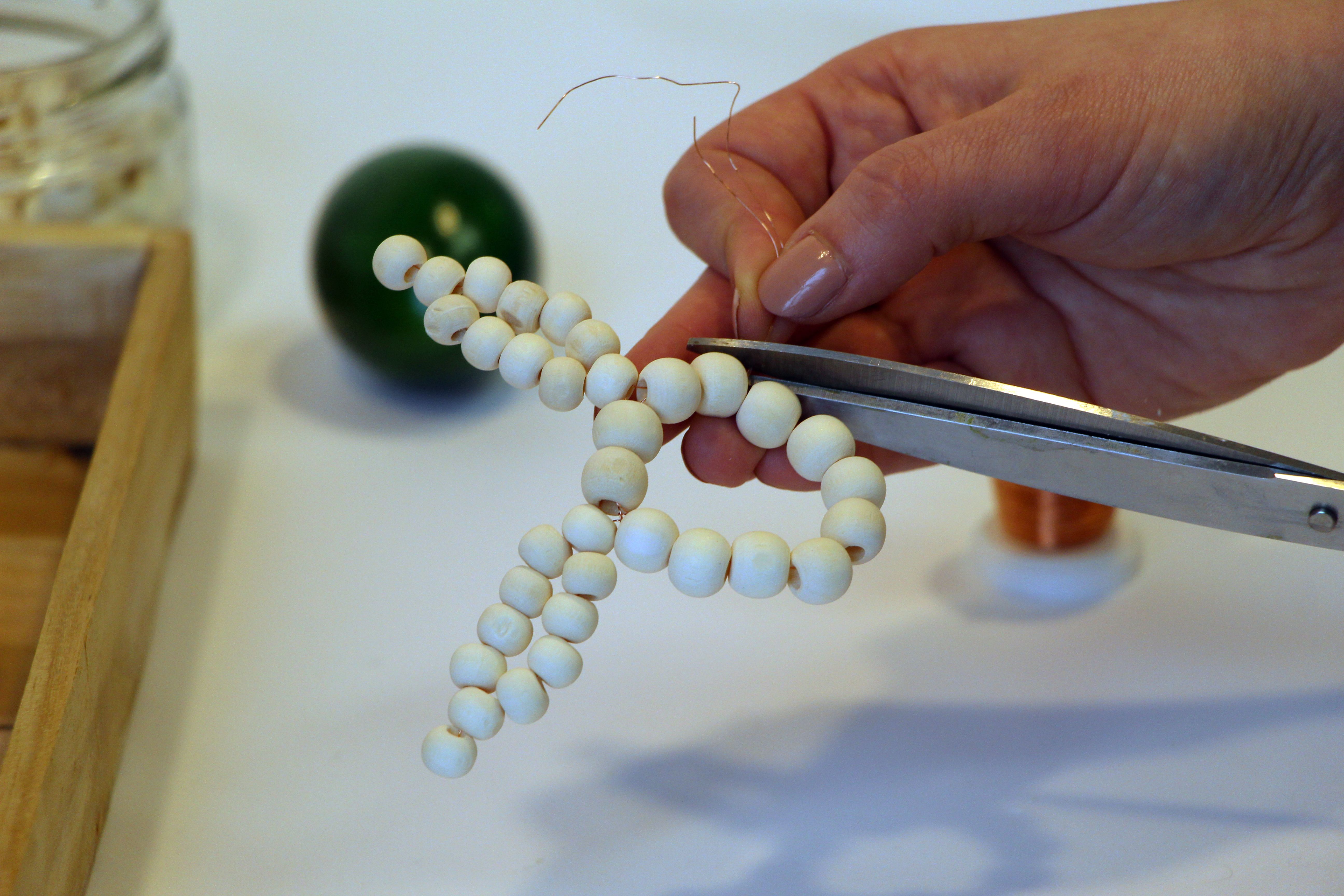 Auf Draht, welcher abgeschnitten wird, sind Holzperlen in Form eines Osterhasen aufgefädelt. 