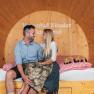 A couple is sitting in a large wooden wine barrel that has been converted into a suite.