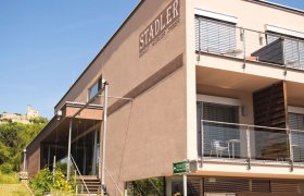 Modernes Gebäude des Weinguts Stadler mit Terrasse und Burg im Hintergrund.