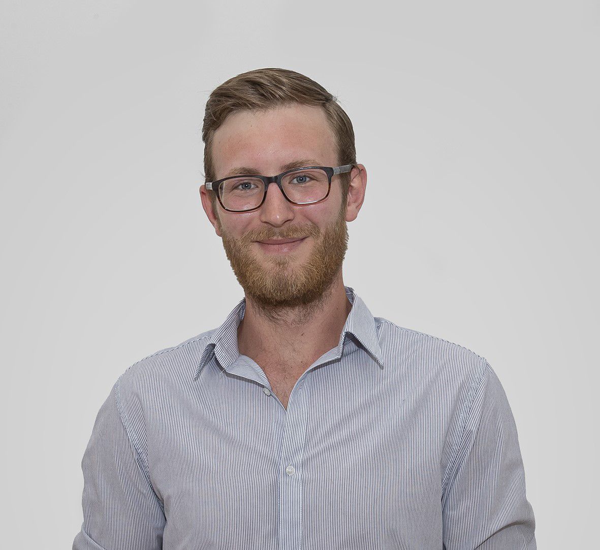 Portrait of a man with glasses and beard in a striped shirt against a neutral background.