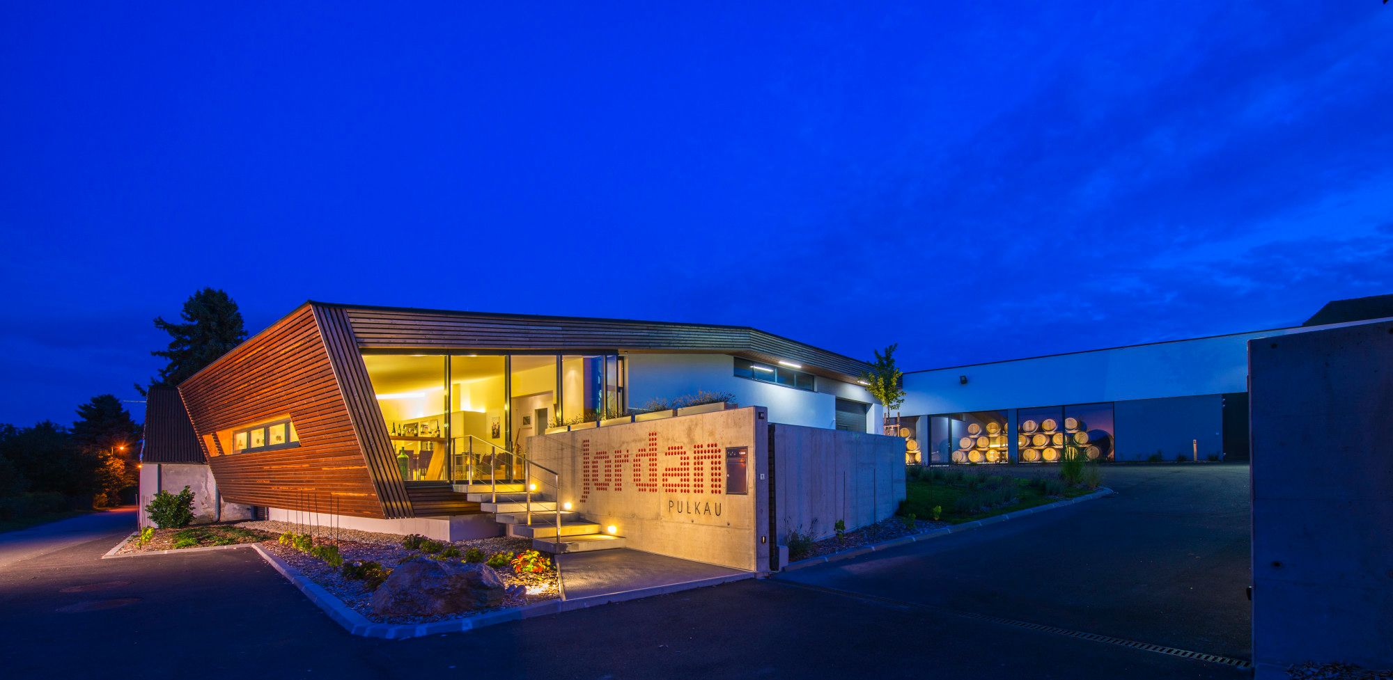 Modernes Weingut bei Nacht mit beleuchtetem Eingang und Holzverkleidung.