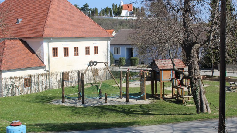 Ein Kinderspielplatz mit Klettergerüst und Schaukel neben einem Gebäude mit rotem Dach.