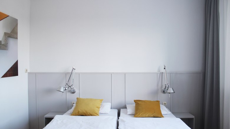 Gästezimmer, © Stadthotel Hollabrunn Modernes Gästezimmer mit zwei Einzelbetten, gelben Kissen und Wandlampen.