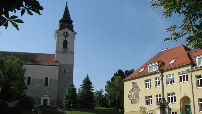 Kirche und Gebäude in Stronsdorf mit Uhrturm und Sonnenschein.