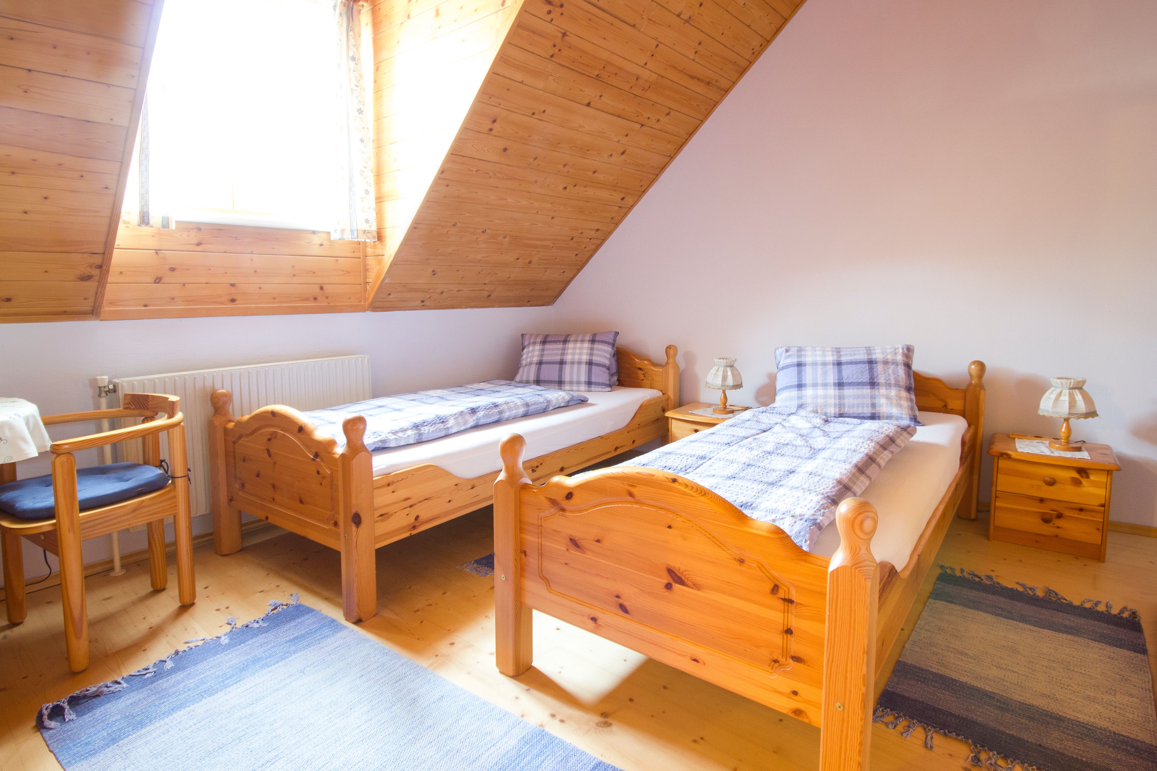 Gemütliches Schlafzimmer mit zwei Einzelbetten aus Holz, blauen Teppichen und einem Fenster mit Holzverkleidung.