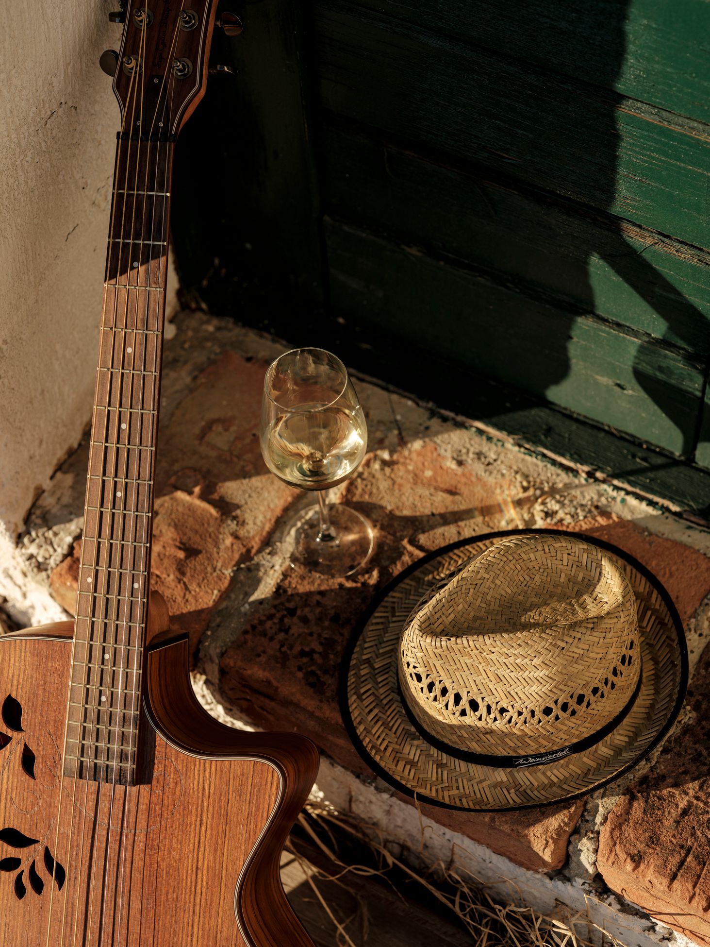 Vor einer Kellertür liegen eine Gitarre, ein Weinviertel Hut und ein Weinglas gefüllt mit Weißwein. 