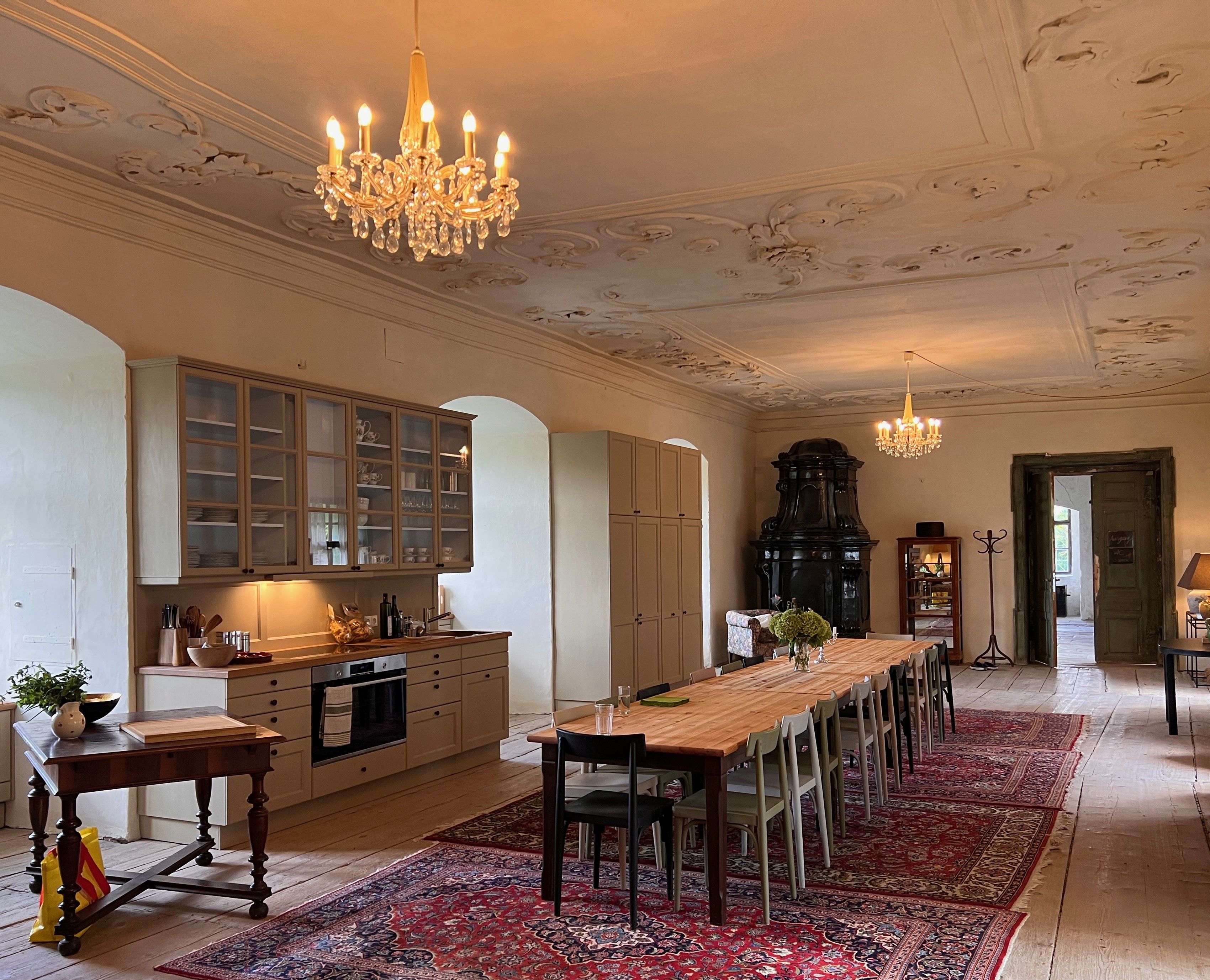 Eleganter Speisesaal mit langem Holztisch, Kronleuchtern und antikem Ofen.