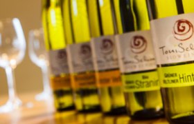 Reihe von Weinflaschen mit Gl&auml;sern im Hintergrund.