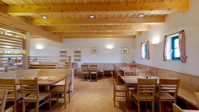 Innenansicht eines gemütlichen Gastraums mit Holzmöbeln und Holzbalkendecke.