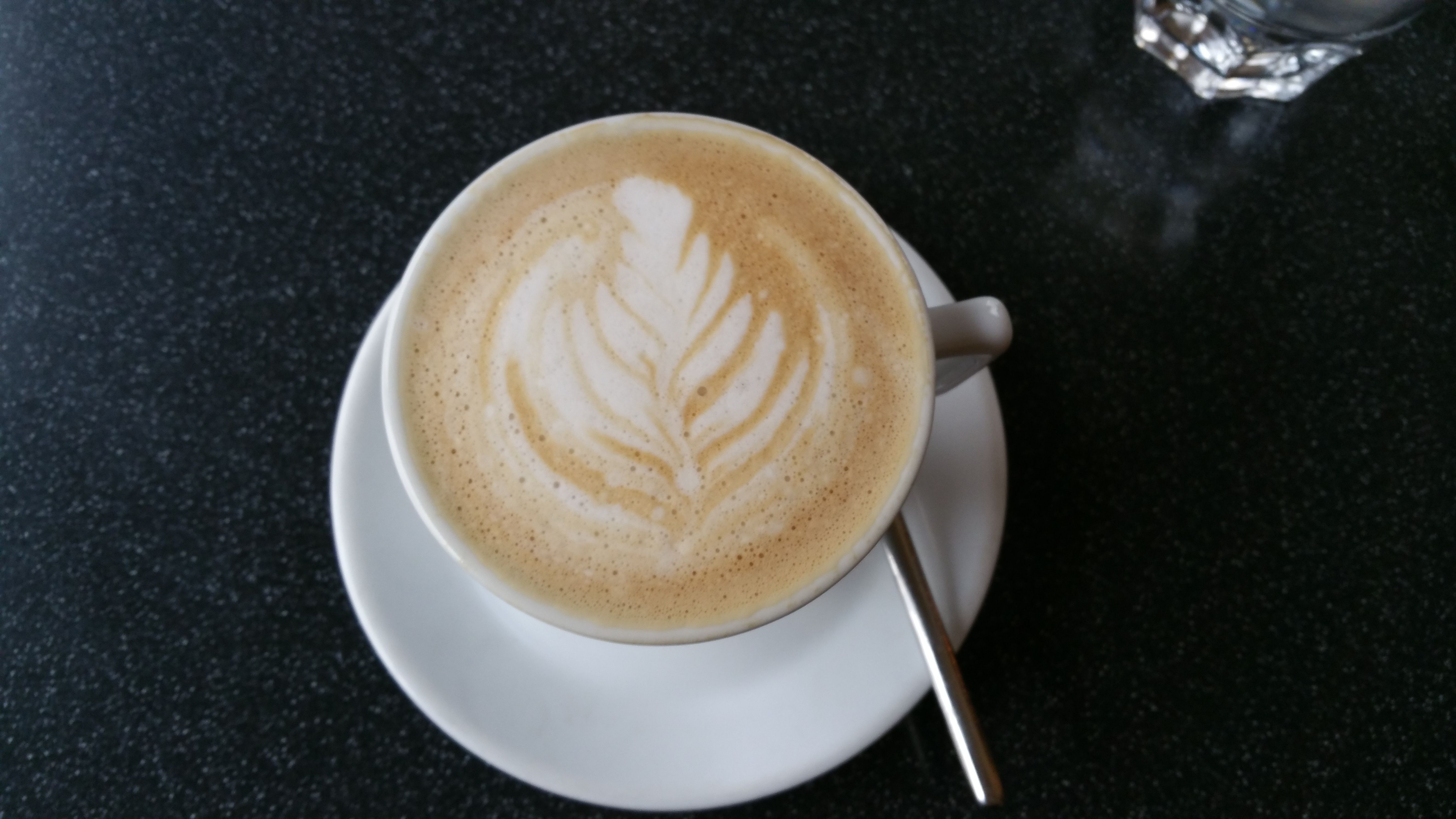 Tasse Cappuccino mit Latte Art auf schwarzem Tisch.