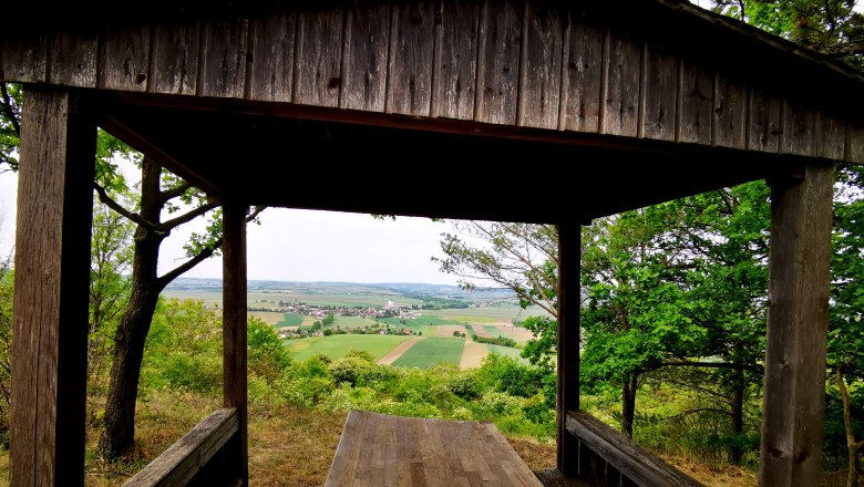 Holzh&uuml;tte mit Blick auf Felder und Dorf in der Ferne.