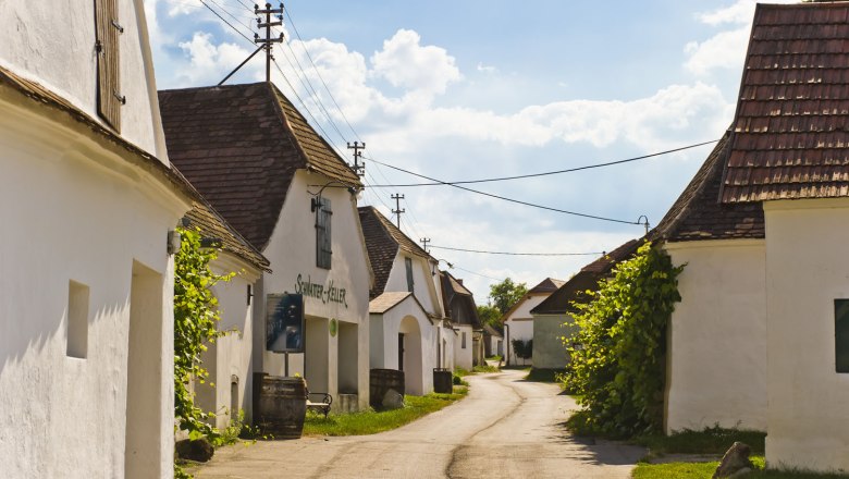 A picturesque wine cellar lane with white buildings and tiled roofs under a blue sky.