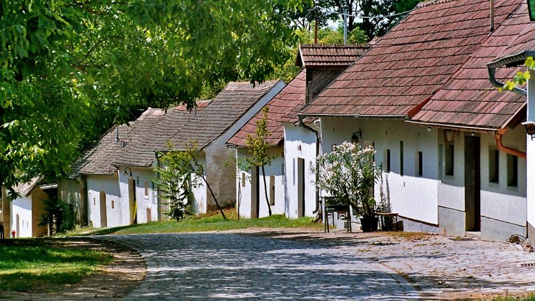 Eine gepflasterte Straße führt an einer Reihe traditioneller weißer Häuser mit roten Dächern vorbei, umgeben von grünen Bäumen.