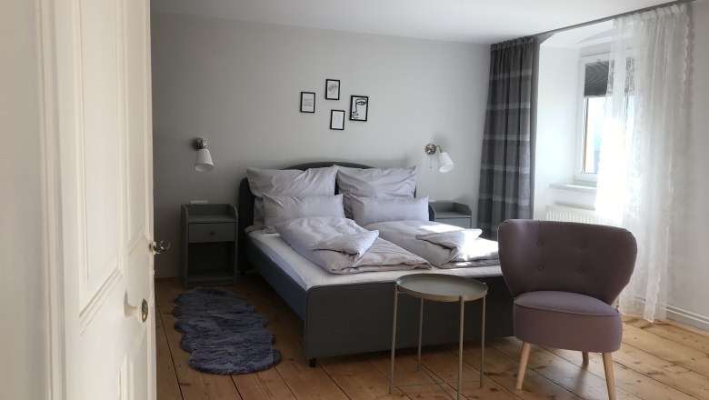 Modern eingerichtetes Doppelzimmer mit Bett, Sessel und kleinem Tisch auf Holzboden.