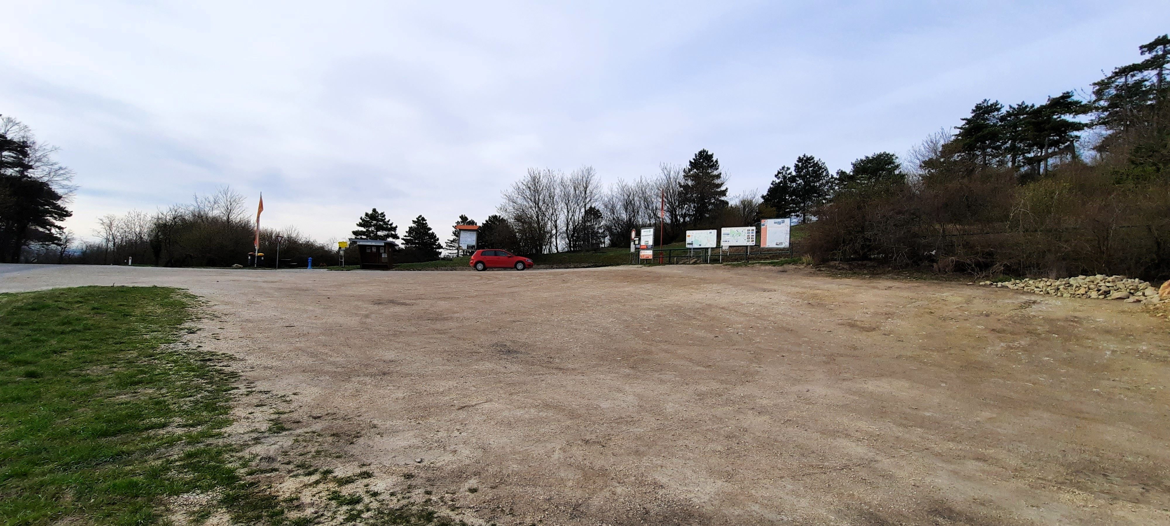 Leerer Wohnmobilstellplatz mit einem roten Auto und Bäumen im Hintergrund.