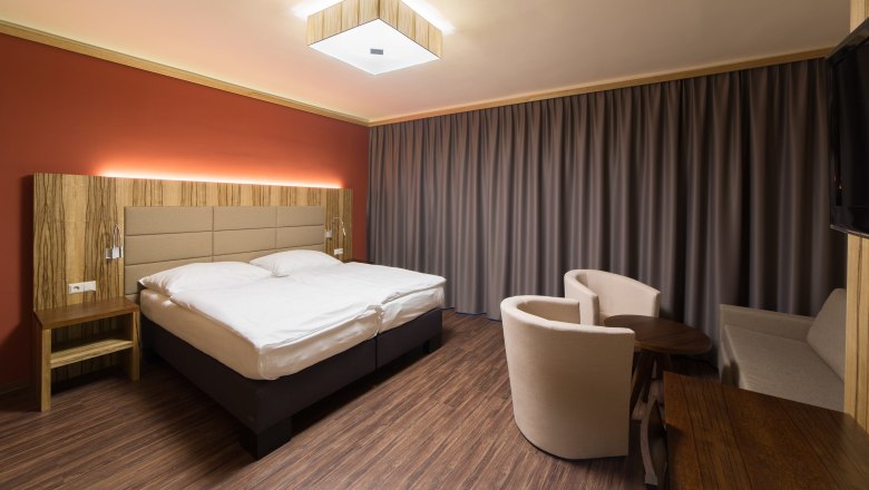 Modern eingerichtetes Hotelzimmer mit Doppelbett, Holzmöbeln und Vorhängen.