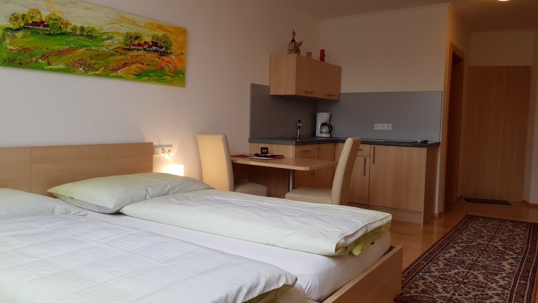 Ein modernes Zimmer mit zwei Betten, einem Schreibtisch, einer kleinen Küchenzeile und einem bunten Gemälde an der Wand.