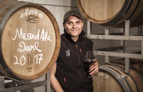 Person in Weinkeller mit Weinglas vor Holzfässern.