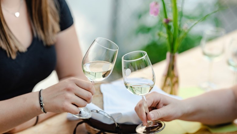 Two people clink glasses of white wine at a table.
